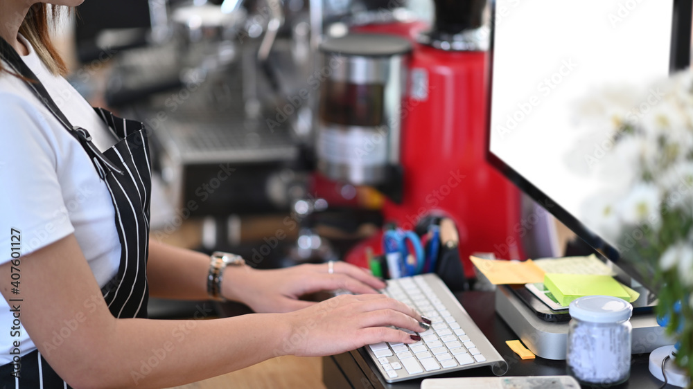 Close up view female entrepreneur in an apron using computer at counter bar in coffee shop. Close up view female entrepreneur in an apron using computer at counter bar in coffee shop.