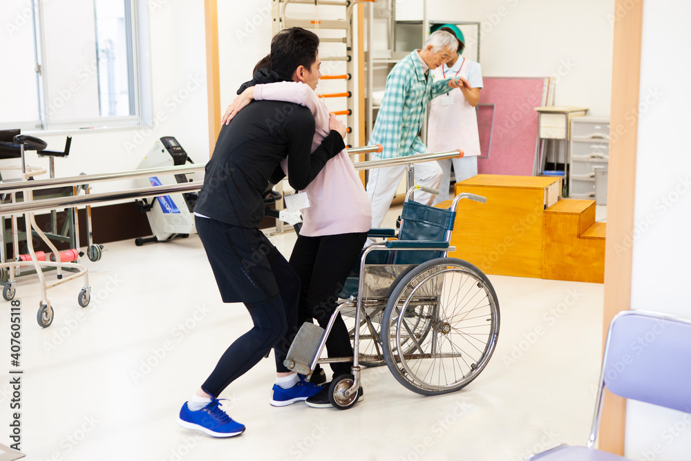 高齢女性を抱きかかえ歩行訓練を補助する男性理学療法士