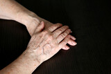Wrinkled hands of elderly woman on a dark wooden table close up. Concept of old age, arthritis, life at retirement
