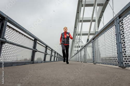 Active senior woman running through the city during the day.