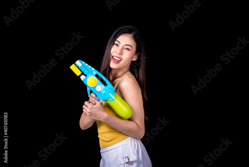 Portrait cheerful young asian woman Wearing a yellow tank top ,holding plastic water gun Smiling and having fun playing in the water Songkran festival, Songkran Thailand. isolated on black background.
