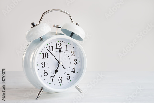 White clock alarm clock showing seven o'clock on a light background with copy space