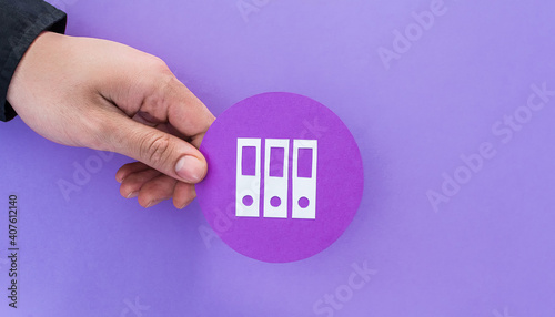 Male hand holding folder shape symbol, on violet background.