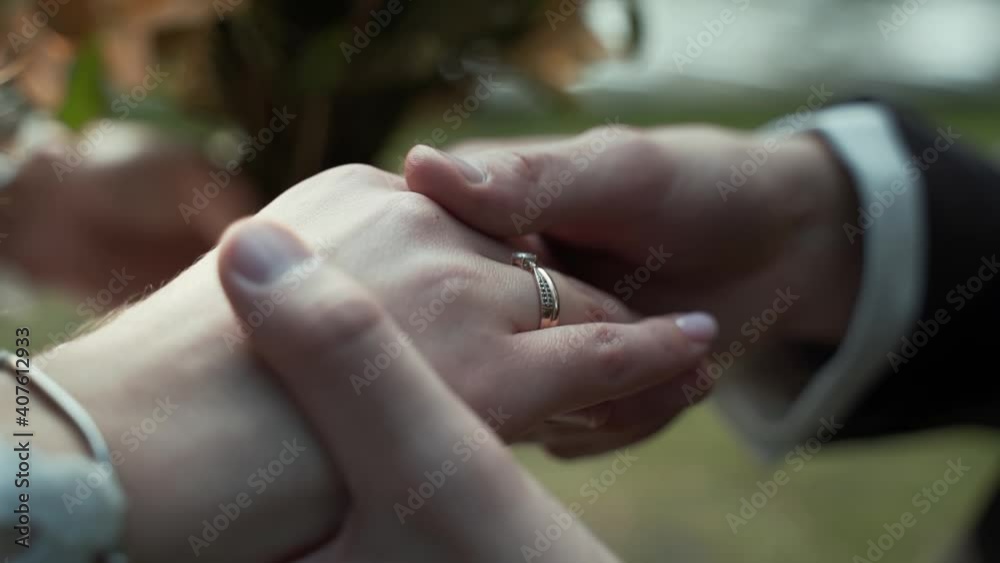 Close-up, caucasian man hands put gold wedding ring on woman finger next to engagement ring on right hand, groom strokes bride hand Close-up, caucasian man hands put gold wedding ring on woman finger next to engagement ring on right hand, groom strokes bride hand