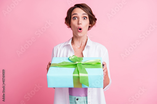 Photo of surprised funny young woman dressed white shirt holding arms teal present box isolated pink color background