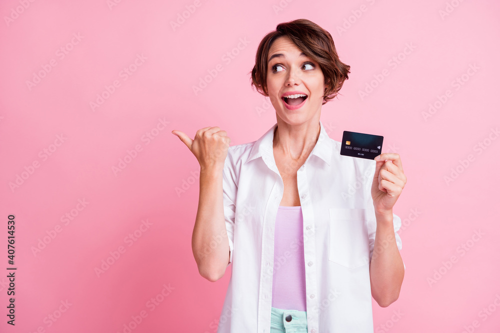 Photo of excited young woman dressed white shirt holding card looking pointing thumb up empty space isolated pink color background Photo of excited young woman dressed white shirt holding card looking pointing thumb up empty space isolated pink color background