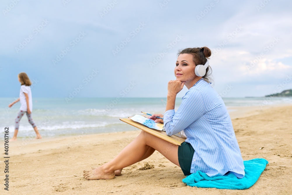 Mature woman sitting on sandy beach drawing sketch of sea