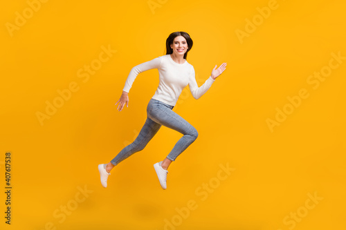 Full size profile photo of optimistic girl jump run wear sweater jeans sneakers isolated on yellow color background