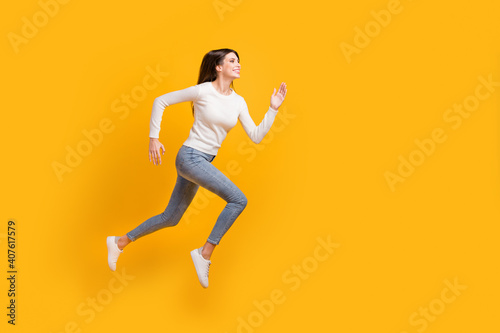 Full size profile photo of optimistic nice girl jump run wear sweater jeans sneakers isolated on yellow color background