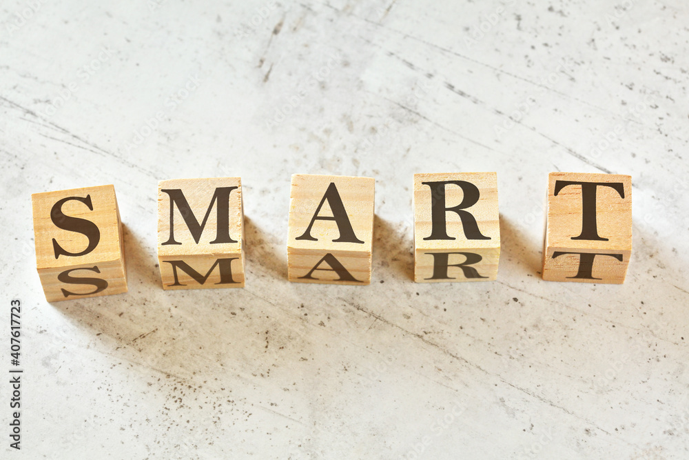 Five wooden cubes with word SMART (means Specific Measurable Attainable Realistic Time bound) on white stone like board, view from above Five wooden cubes with word SMART (means Specific Measurable Attainable Realistic Time bound) on white stone like board, view from above