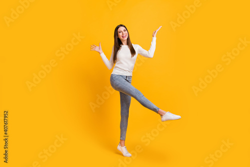 Full size photo of optimistic brunette girl dance wear sweater jeans sneakers isolated on yellow color background