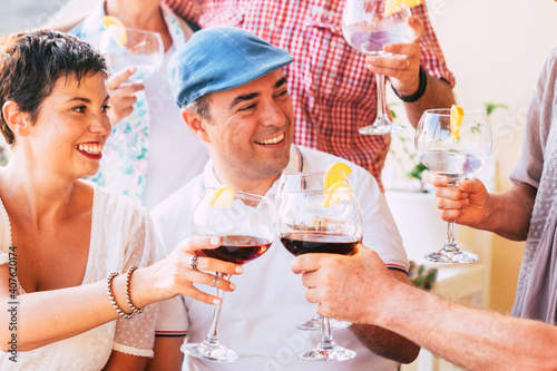 Group of cheerful caucasian friends enjoy and celebrate together clinking with red wine and cocktails glasses - people celebrate and enjoy friendship with smile and fun in daylight