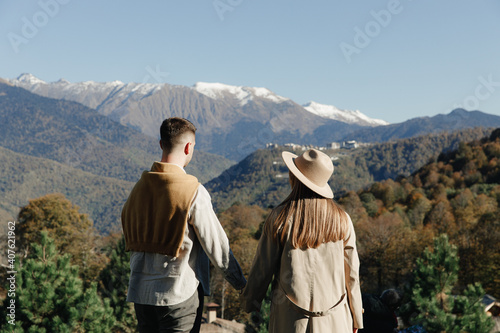 Happy couple in love are walking in fashion autumn clothes on the background of nature mountains landscape, holding hands and having fun. Date when quarantine and self-isolation