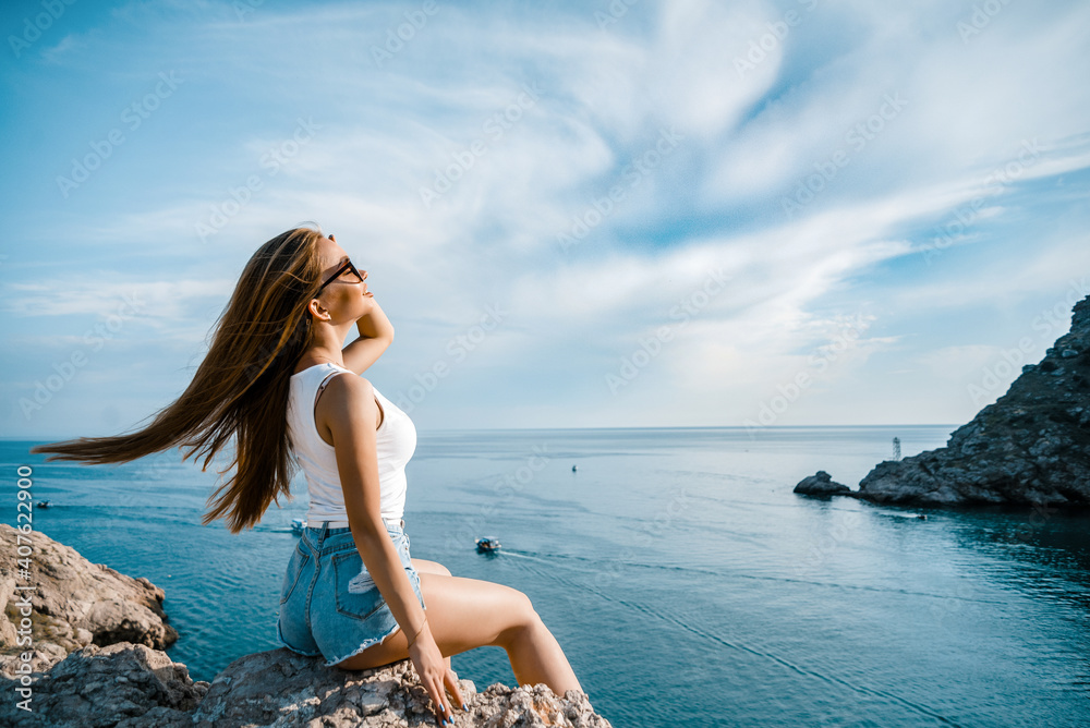 Joyful woman travel mountains. Authentic blond female relax in picturesque landscape. A girl with developing natural hair is wearing a white top and denim shorts. Joyful woman travel mountains. Authentic blond female relax in picturesque landscape. A girl with developing natural hair is wearing a white top and denim shorts.