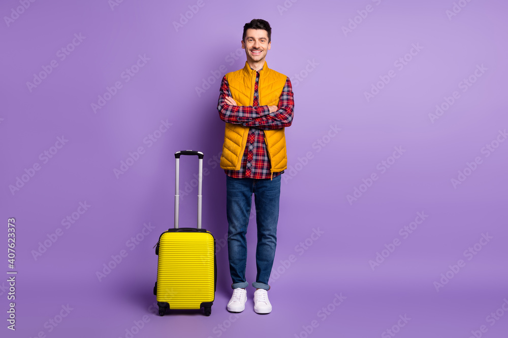 Full length photo of positive confident young guy dressed yellow vest hands arms crossed luggage isolated purple color background Full length photo of positive confident young guy dressed yellow vest hands arms crossed luggage isolated purple color background
