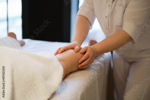 Detail of hands massaging human calf muscle.Therapist applying pressure on female leg. Hands of massage therapist massaging legs of young woman in spa salon. Body care in spa salon for young woman. © yavdat