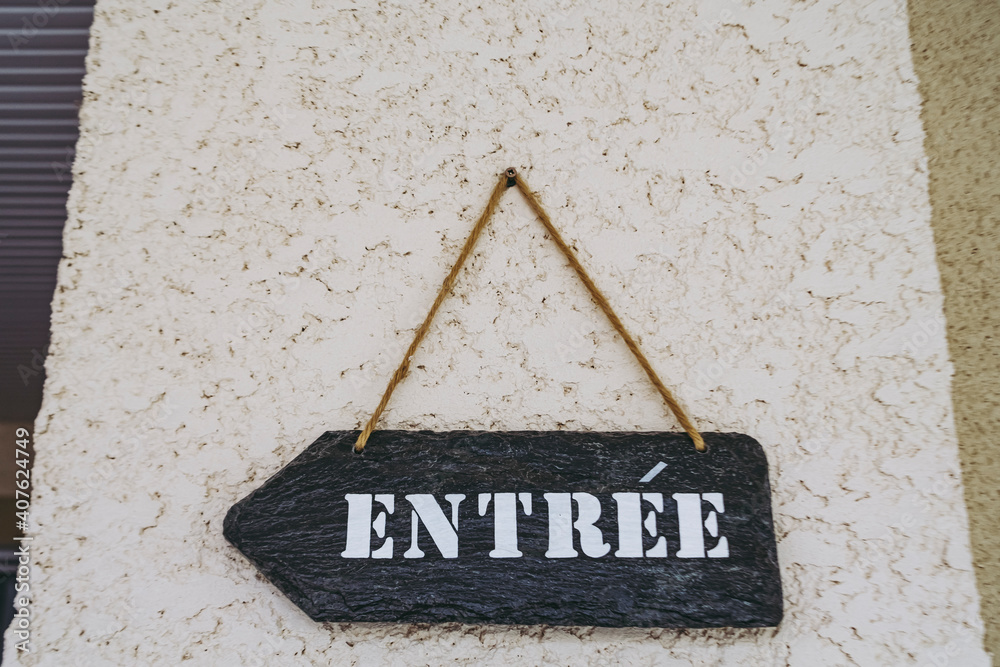 Panneau en forme de flèche avec le mot entrée en français sur une façade de maison foto de Stock