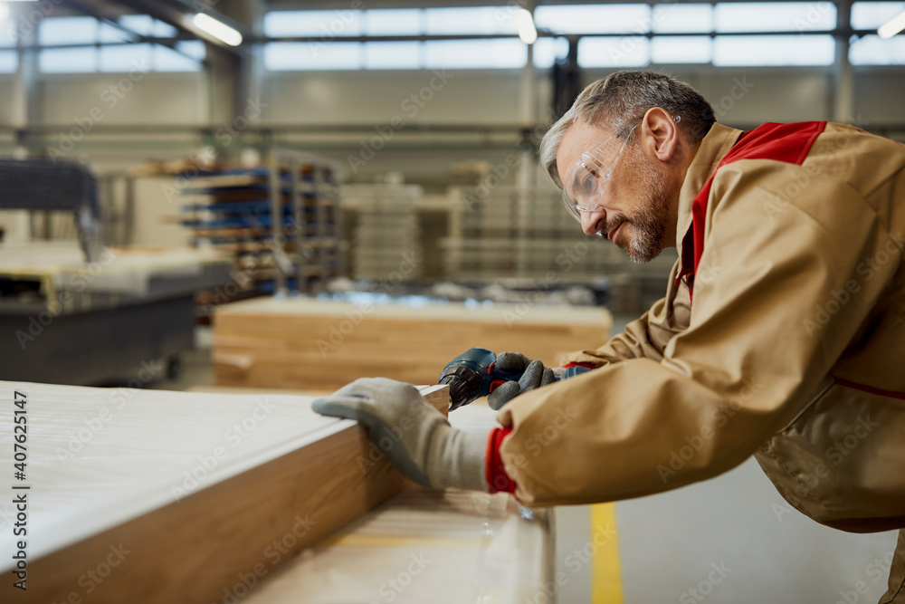 Male worker using a drill while making furniture in carpentry workshop.