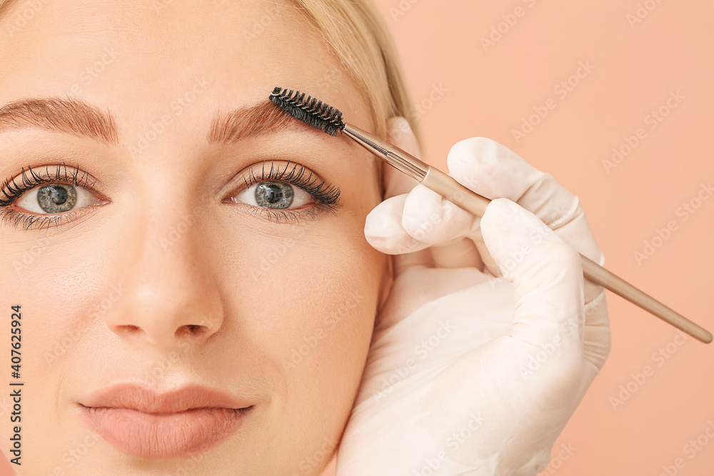 Young woman undergoing eyebrow correction procedure on color background