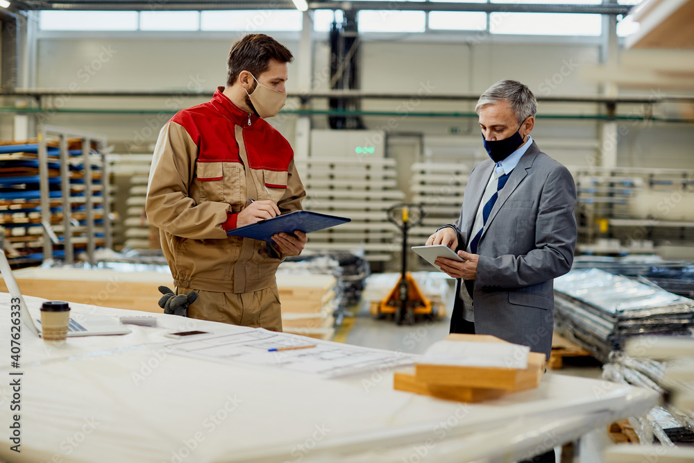 Project manager using touchpad while talking to a worker at carpentry workshop during coronavirus pandemic. Project manager using touchpad while talking to a worker at carpentry workshop during coronavirus pandemic.
