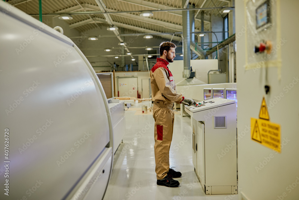 Full length of a worker using automated machine at woodworking production facility. Full length of a worker using automated machine at woodworking production facility.