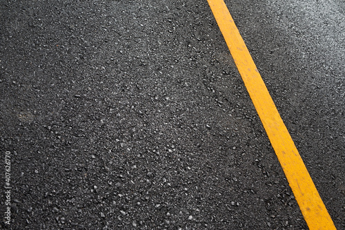 Close up black asphalt road surface texture with a yellow line. © Thawatchai