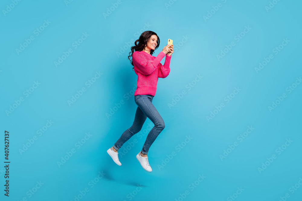 Full body profile side photo of happy brunette wavy haired girl hold phone go copyspace jump isolated on blue color background