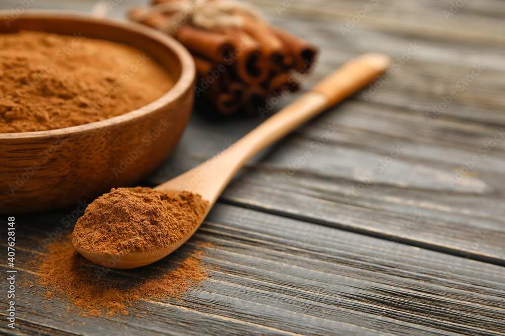 Bowl and spoon with cinnamon powder on wooden background