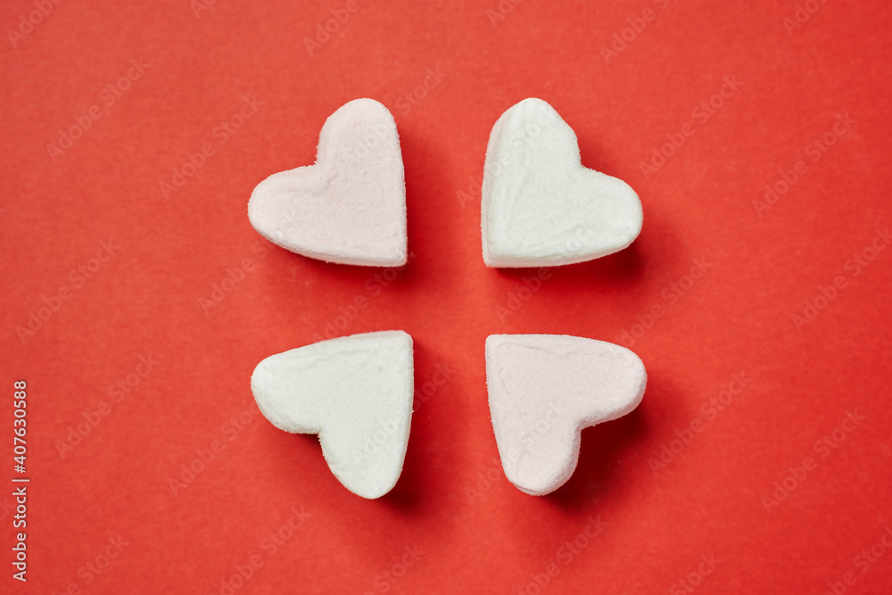 Fototapeta premium in the center of the red background, four white and light pink marshmallows in the form of a heart