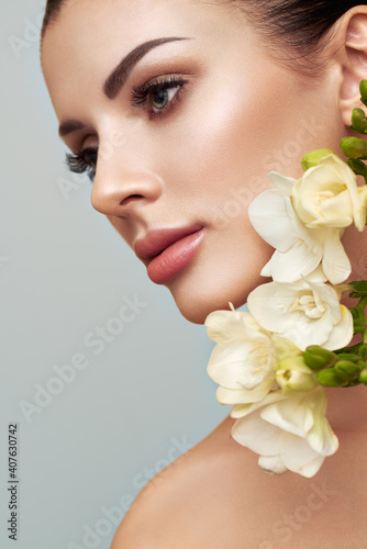Beautiful model with a flower. Perfect woman face makeup close up. Lipstick. Eyelashes. Glowing skin