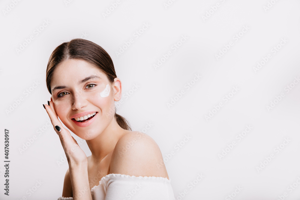 Girl touches moisturized skin and smiles. Portrait of model with cream on face on isolated background Girl touches moisturized skin and smiles. Portrait of model with cream on face on isolated background