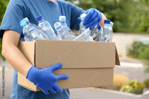 Woman holding cardboard box with used plastic bottles outdoors, closeup. Recycling problem © New Africa