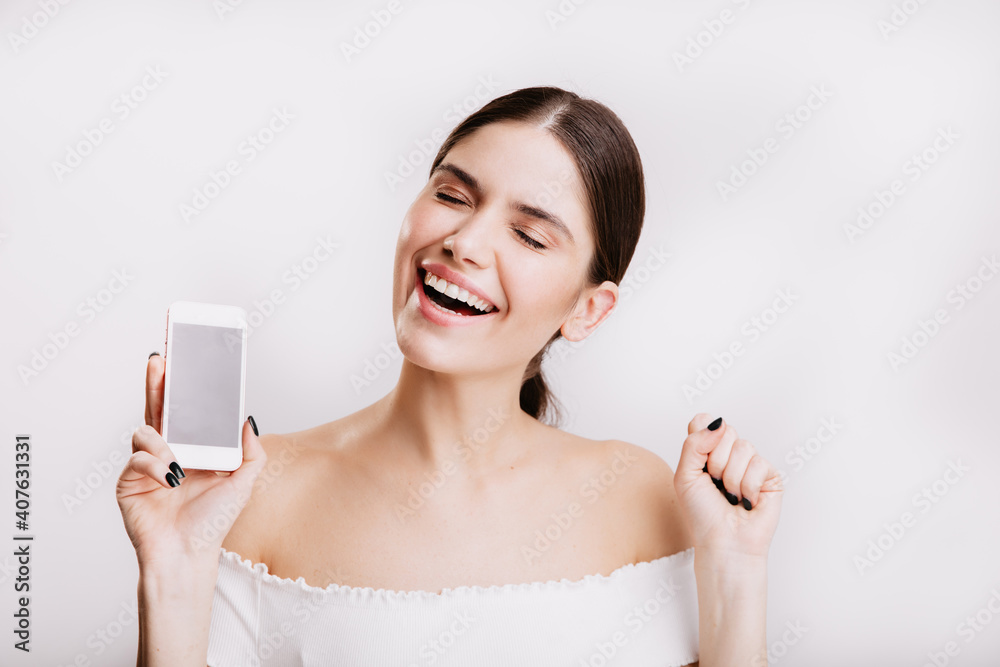 Happy woman with snow-white smile rejoices on white background, holding her new phone Happy woman with snow-white smile rejoices on white background, holding her new phone
