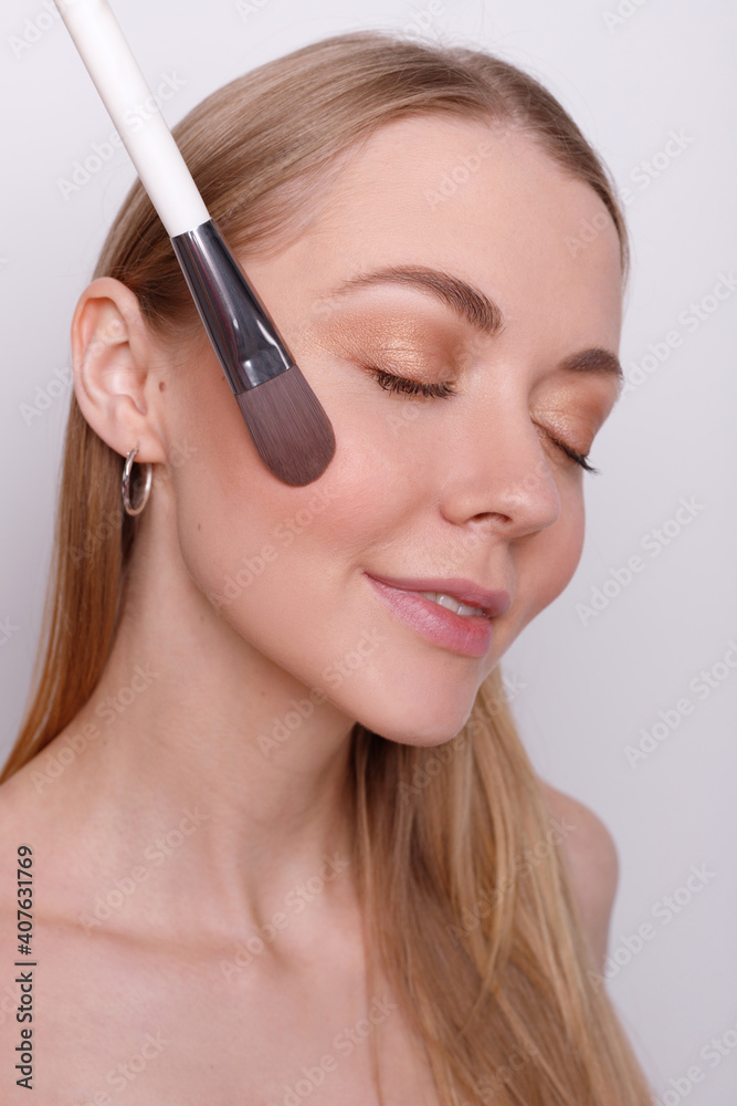 Girl with a brush for makeup on the face on a gray background
