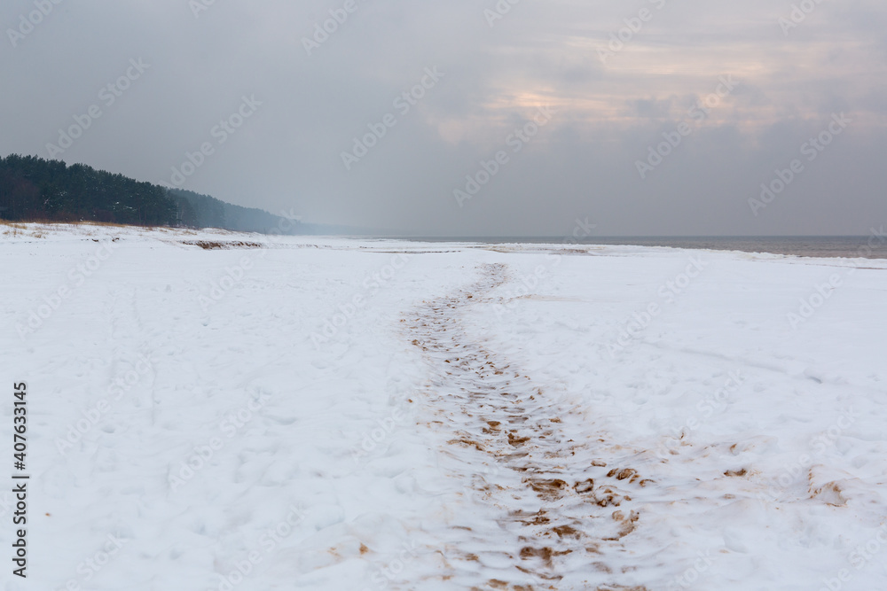 Calm winter seaside scene with footprints in snow at the Baltic sea on a cloudy day in January in Saulkrasti in Latvia