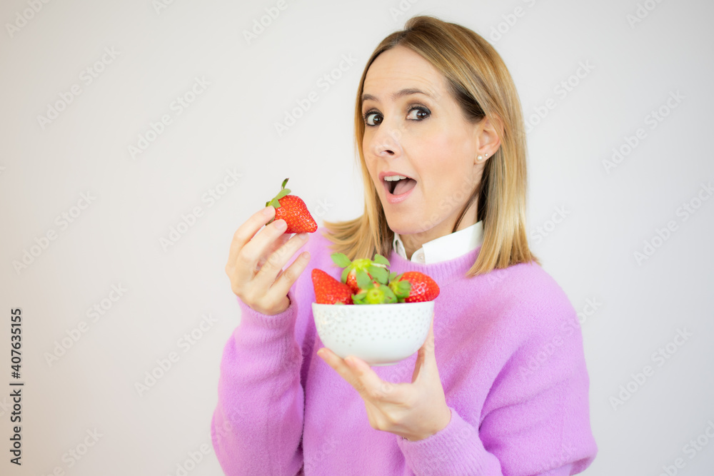 Beautiful cheerful young woman standing and holding glass bowl with strawberries over white background Beautiful cheerful young woman standing and holding glass bowl with strawberries over white background