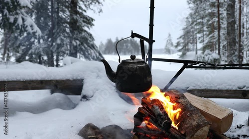 Coffee pot hanging over the fire outside in the winter forest. Winter theme. Camping, hiking concept. 
