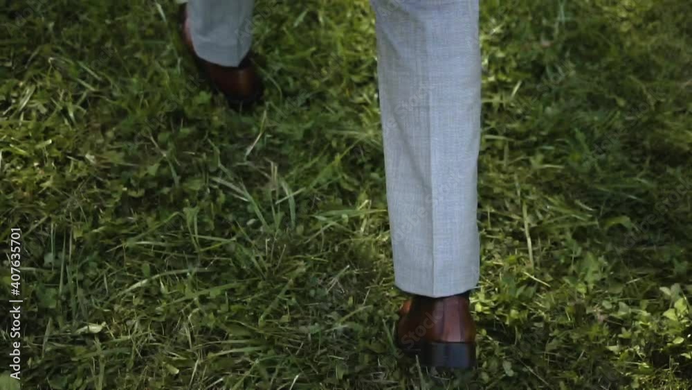 A caucasian man in a gray elegant suit and brown polished shoes walks on the fresh green grass and carries a delicate bouquet of white peonies A caucasian man in a gray elegant suit and brown polished shoes walks on the fresh green grass and carries a delicate bouquet of white peonies