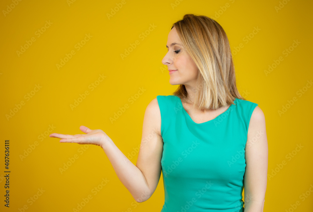 Portrait of smiling woman showing something or copy space for product or sign text, isolated over yellow background Portrait of smiling woman showing something or copy space for product or sign text, isolated over yellow background