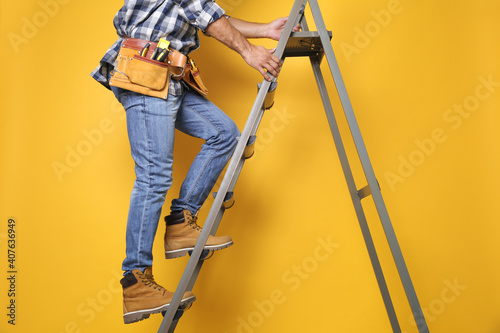 Professional builder climbing up metal ladder on yellow background, closeup photo