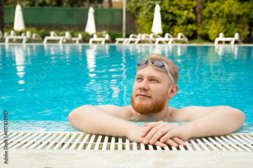 young man with beard rest in the pool with swimming goggles by the hotel