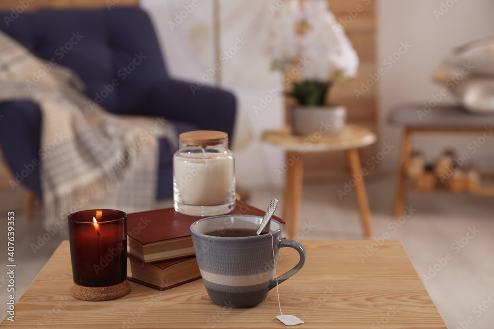 Cup of tea, books and candles on wooden table in living room. Interior design Cup of tea, books and candles on wooden table in living room. Interior design