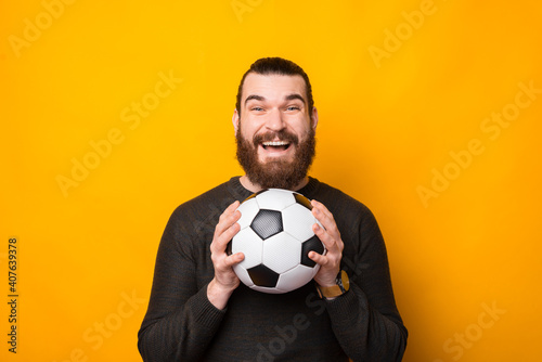 Portrait of happy bearded man holding soccer ball over yellow background. © Vulp