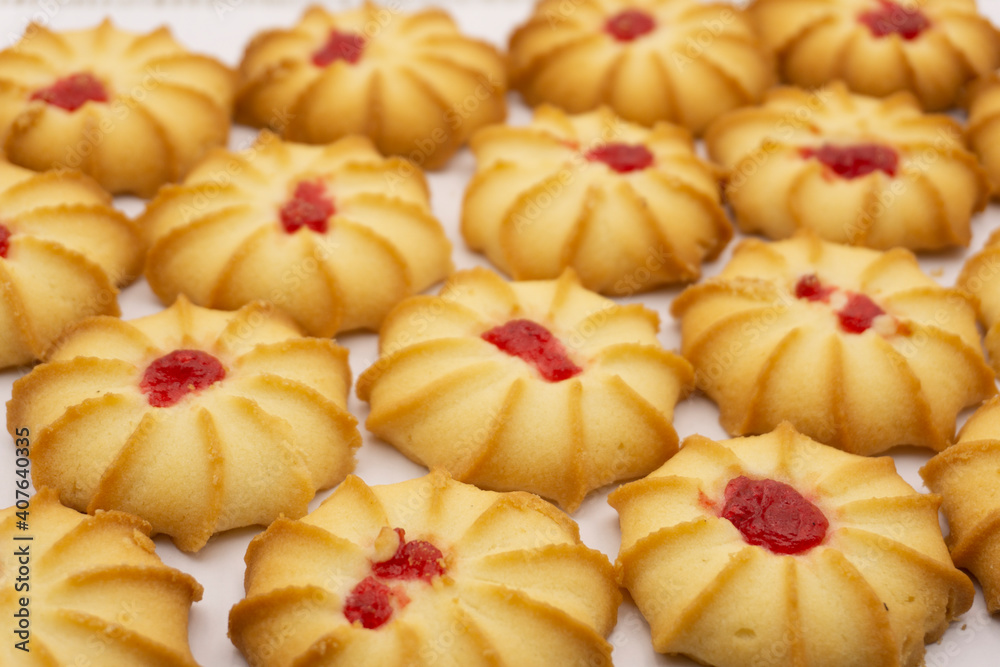 Shortbread cookies with jam in the middle on white plate against brown background .