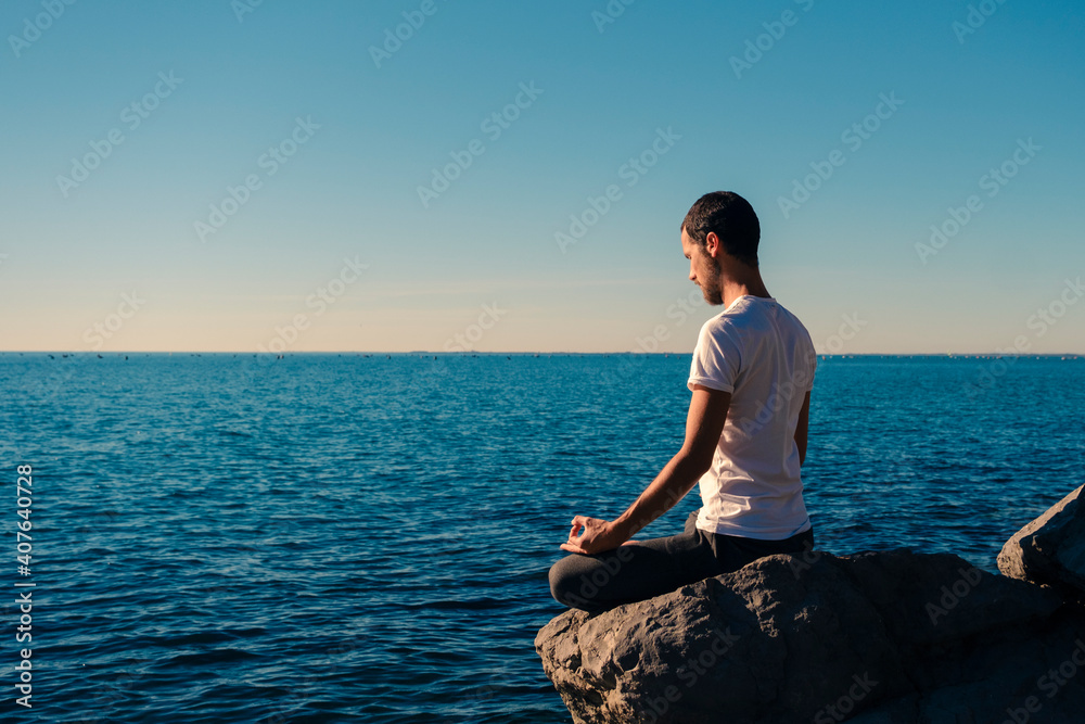 Attractive young man practicing yoga meditation and breathwork outdoors by the sea