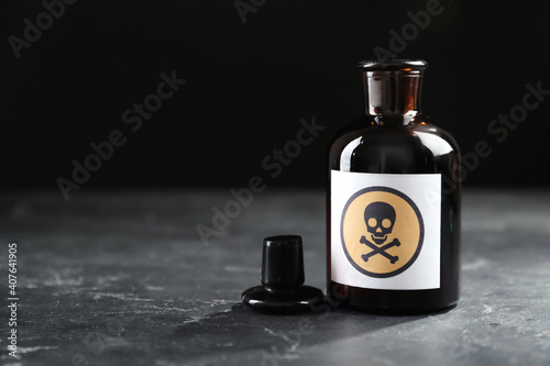 Open glass bottle of poison with warning sign on black table. Space for text