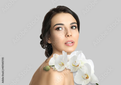 Beautiful young woman and orchid flowers on light background. Spa portrait