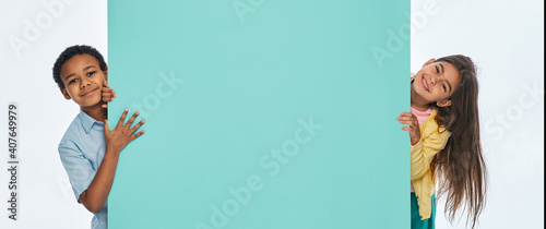 Canvas Print Multi-ethnic children peeking from behind an empty turquoise wall