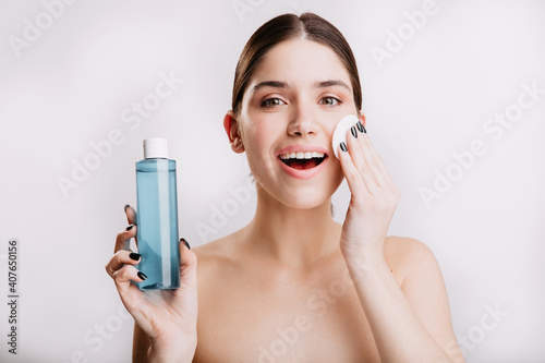 Beautiful woman delicately moisturizes skin with cosmetic tonic. Portrait of lady with healthy skin without makeup on isolated background