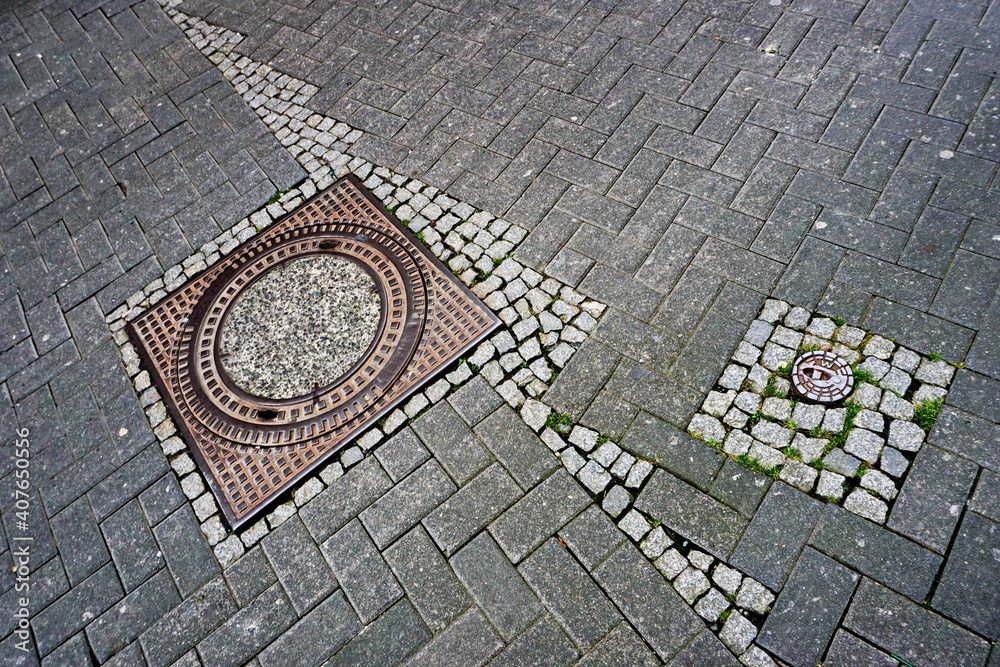 Old pavement in the city. A sewer manhole and a small cobblestone. A combination of a square ..and a circle.